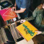 ue persone sfogliano dischi in vinile vintage in un negozio di dischi, luce calda e atmosfera retrò. - Foto U+
